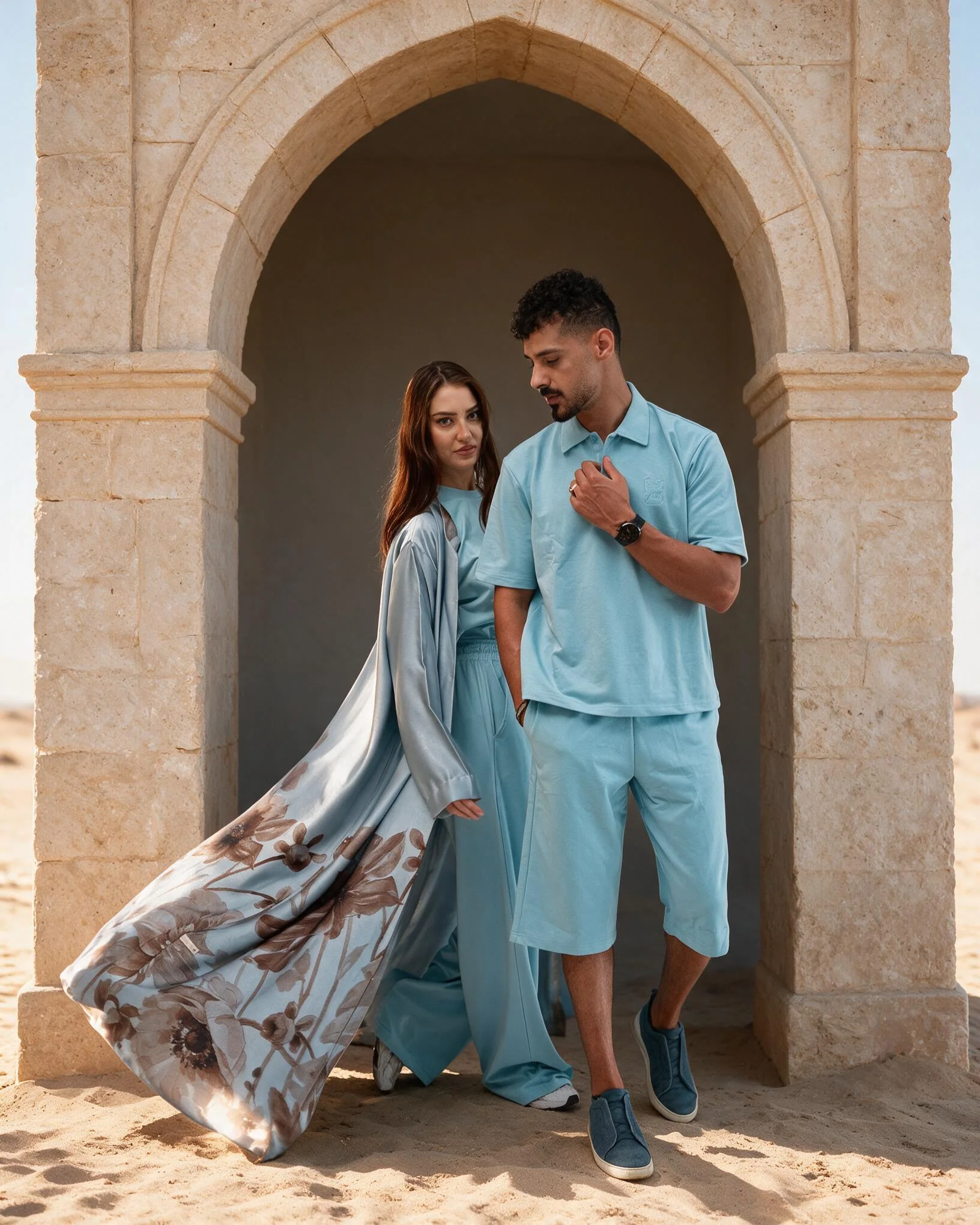 Couple dressed for Eid, a flowing printed abaya over a blue set and a light blue polo with shorts